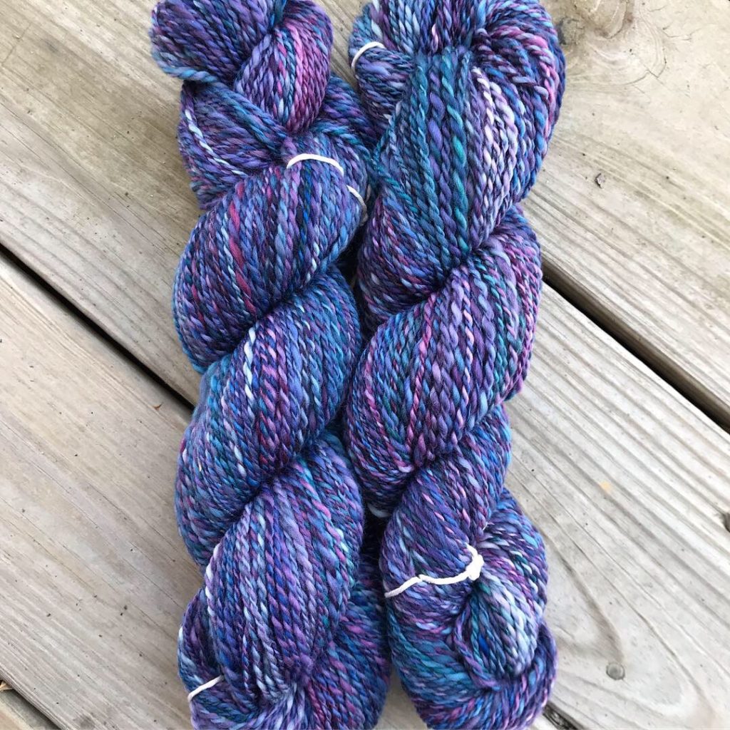 two skeins of handspun yarn in deep blues and purples, lying on wooden planks