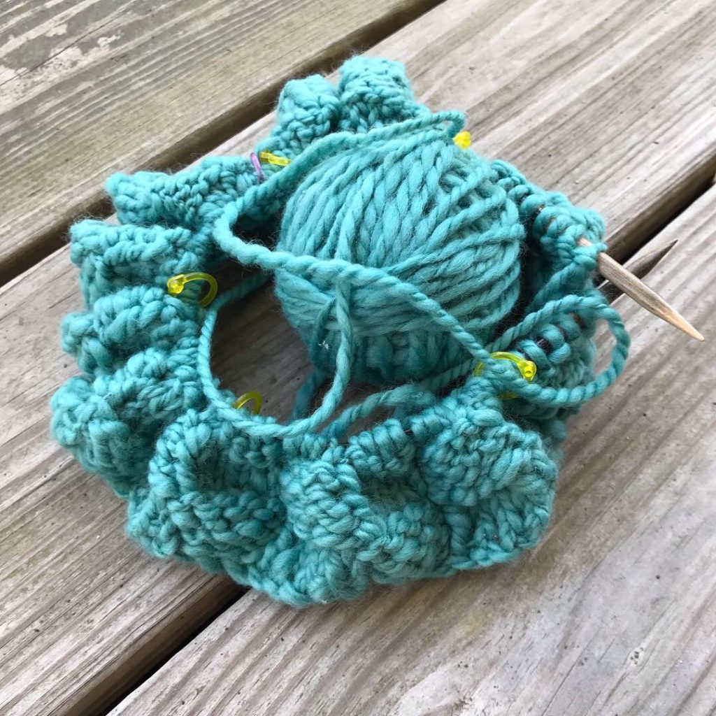 Ball of handspun yarn and handknit cowl in progress, on wooden circular needles.